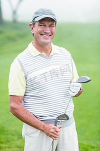 高尔夫球杆图形摄影照片_快乐的高尔夫球手拿着他的球杆对着镜头微笑