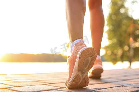 跑步者的脚在日落或日出时在户外的鞋子上跑在道路特写上。