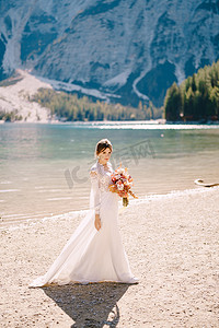 玫瑰干花摄影照片_美丽的新娘穿着白色的袖子和蕾丝连衣裙，带着一束黄色的秋干花和牡丹玫瑰，在意大利的布拉伊斯湖上。