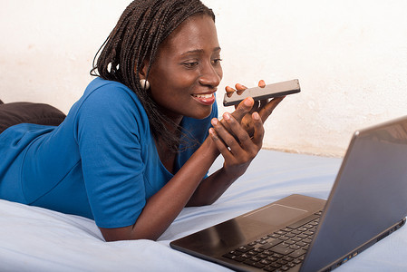 手机文案摄影照片_年轻微笑的女人在床上用手机聊天