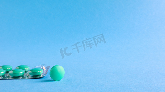 麻醉摄影照片_一个银色泡罩，上面有圆形绿色药丸和一个圆形药片，放在蓝色背景上。