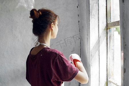 室内装修中摄影照片_穿白围裙的女人在房屋室内装修中画窗户
