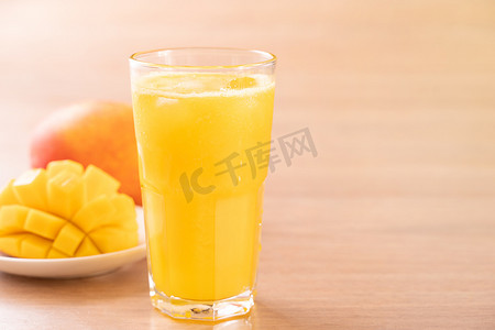 芒果摄影照片_明亮的木桌背景上有漂亮的切碎果肉的新鲜芒果汁。