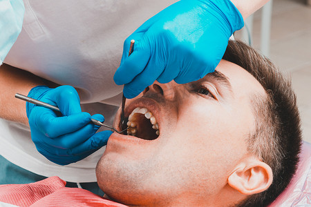 评估诊断摄影照片_牙科诊所，病人坐在牙科椅上，张大嘴巴，牙医评估牙齿状况并做出诊断。