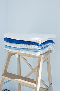 松毛汤包摄影照片_一堆干净的浴巾彩色棉毛圈纺织品堆放在木椅上，靠近白墙堆概念特写