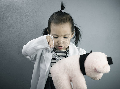 学校职业摄影照片_亚洲小女孩角色扮演医生职业，穿着白色礼服制服，注射毛绒玩具熊。