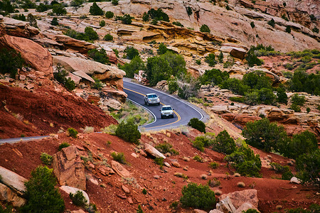 在有岩石峭壁的红沙沙漠山谷风景秀丽的弯曲道路上行驶的汽车
