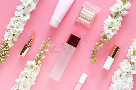 桌面背景粉摄影照片_面部化妆品美容产品与柔和的粉红色桌面背景上的白花。