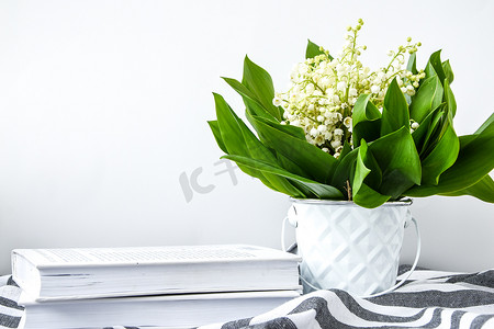 一束铃兰放在白色的桶里，白色的桌子上放着书籍，有复制空间。
