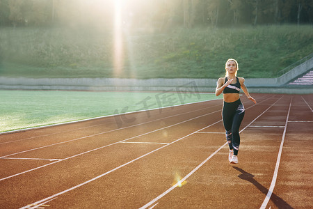 在体育场运动跑道上做有氧运动的黑色运动服跑步白人女性的前视图。