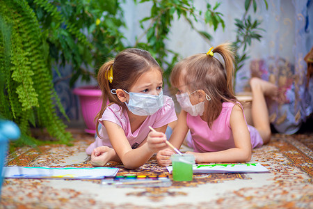 两个戴着医用防护口罩的悲伤女孩在家里或幼儿园的地板上涂漆。