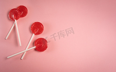 粉色柔和背景上的圆形红色甜美味棒棒糖。