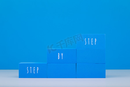 由蓝色块制成的梯子，在蓝色背景下写有逐步文本，并带有复制空间