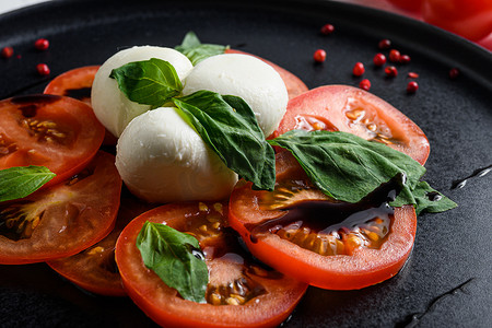 Caprese 新鲜意大利沙拉配西红柿、马苏里拉奶酪、深色石板上的绿色罗勒，白色背景选择性聚焦特写