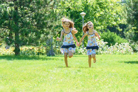 两个小妹妹在公园的绿色草坪上奔跑