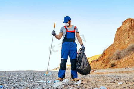 男子志愿者用伸展杆在海滩上收集垃圾