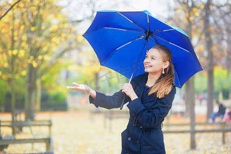 带伞的女孩摄影照片_巴黎卢森堡花园秋春雨天带蓝伞的年轻女子