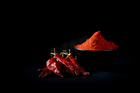 红黑色背景摄影照片_黑碗里的冷粉，黑色背景上有红冷、干辣椒