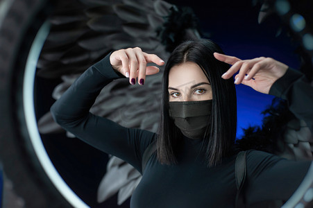 疾病预防背景摄影照片_黑色翅膀背景中的黑发女性，戴着防冠状病毒的防护面具，手画像