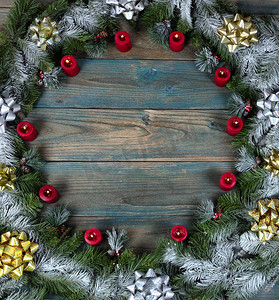蝴蝶结边框摄影照片_圣诞节或新年背景的冬季假期，雪覆盖的花环的顶视图，上面有发光的红色蜡烛装饰品，加上蓝色老化木板上圆形边框的蝴蝶结