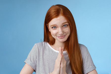 可爱的女孩表演善良的天使凝视着镜头傻笑着问请帮忙合掌祈祷瞥一眼轻浮乞讨站在蓝色背景恳求真诚借衣服