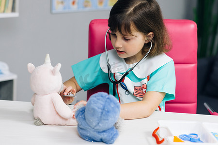 可爱的小女孩穿着医疗服玩游戏，作为兽医拿着听诊器听生病的玩具。