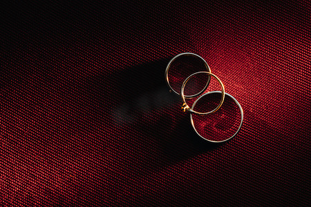 枚红色摄影照片_红色背景上的两枚结婚戒指和一枚订婚戒指。