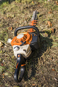 发动机汽油发动机摄影照片_橙色汽油发动机便携式电锯在草地上。