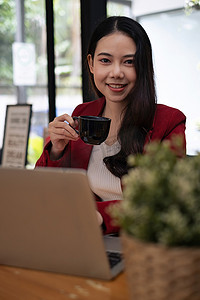 美丽的基金经理坐在椅子上，在咖啡馆的木桌上放着一杯咖啡和平板电脑。