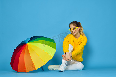 身穿黄色毛衣、带五彩伞的女人摆出彩虹色