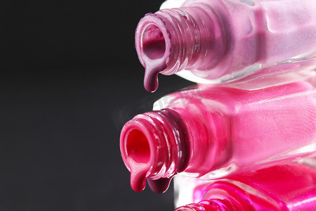 粉色化妆品瓶子摄影照片_黑色深色背景中，带有复制空间的红色胡须粉红色指甲油从瓶子的瓶子里流出