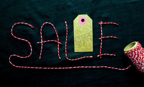 销售，折扣词由红线制成，黑色背景上有一个线轴。