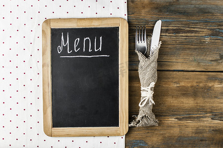 设置的标摄影照片_菜单标题写在黑板上的白色粉笔与桌子设置刀叉躺在桌布圆点上。