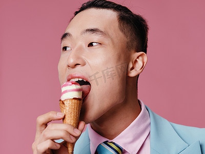 蓝色经典西装裁剪视图中粉红色背景中吃冰淇淋的快乐亚洲男人
