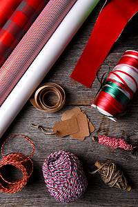 条纹和格子摄影照片_平铺在质朴的木质表面上的圣诞礼物包装纸、丝带和绳子。