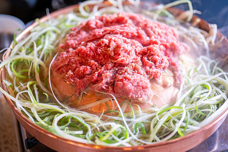 韩国烤肉摄影照片_首尔韩国餐厅的牛肉烧烤烤肉，铜锅上的生活方式新鲜韩国美食，配上葱片，特写，复制空间
