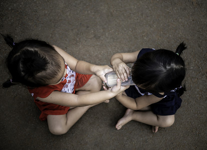 亚洲小孩坐在花园里，用玻璃杯给妹妹喂牛奶