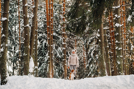 一个冬天的女人和她的宠物狗比格犬在冬季森林里玩耍