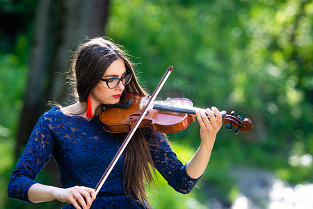 湖畔小提琴摄影照片_在公园拉小提琴的年轻女子。