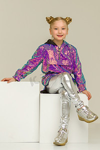 小女孩盘腿坐在白色立方体上。