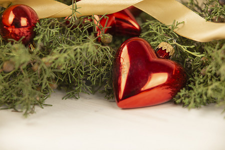 木质背景上带有松树枝、红色小饰物和缎带金丝带的土形圣诞红色小饰物的特写，具有散景效果