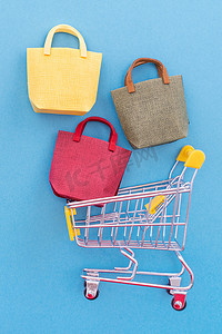 抽象设计元素，年度销售，购物季节概念，带有彩色纸袋的迷你黄色购物车，柔和的蓝色背景，顶视图，平躺