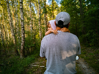 爸爸怀里可爱的小孩在公园里抱着他的脖子.