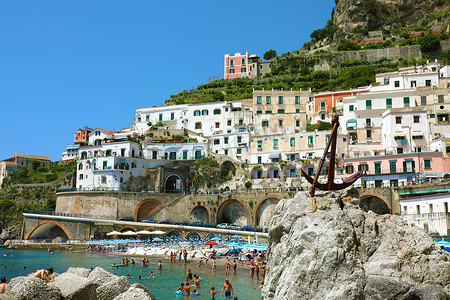 锚定摄影照片_意大利阿特拉尼-2018 年 7 月 2 日：在意大利阿马尔菲海岸阿特拉尼的海滩上锚定在石头和人们身上