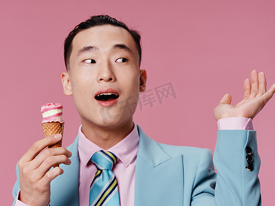 韩国经典摄影照片_穿着蓝色经典西装的粉红色背景中吃冰淇淋的快乐亚洲男人特写