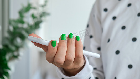 指甲摄影照片_修剪整齐的女性手与时尚的绿色指甲拿着手机。