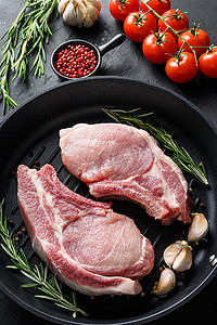 肉排摄影照片_生猪里脊肉排在煎锅附近的配料中，配以香草胡椒和西红柿，俯视垂直选择性焦点