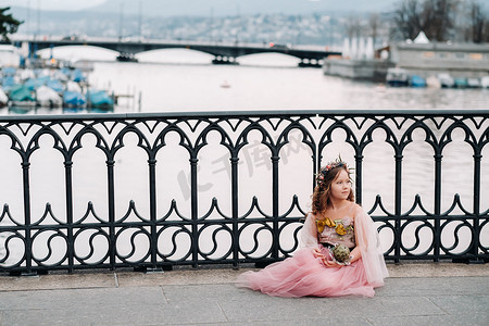 粉色裙摄影照片_一个穿着粉红色公主裙的小女孩手里拿着一束花穿过苏黎世老城。瑞士城市街道上一个穿着粉红色连衣裙的女孩的肖像
