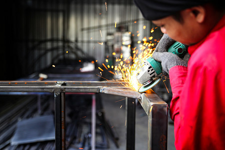 焊工在工厂用火花在钢材上使用磨石，在工业车间进行焊接工艺，手在框架中使用仪器。