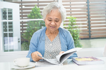 老年大脑摄影照片_亚洲老年或老年老太太在家中读书练习大脑，休息爱好退休概念。